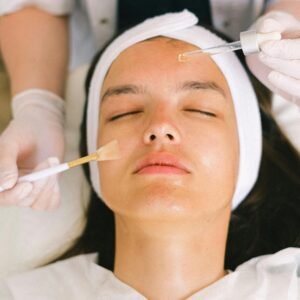 Top view skilled female cosmetologist in uniform and gloves applying essential oil on young woman face skin while working in contemporary spa center